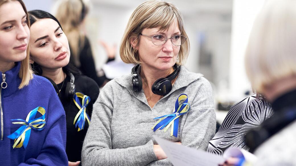 Women with blue and yellow ribbons gather, one holds a paper.