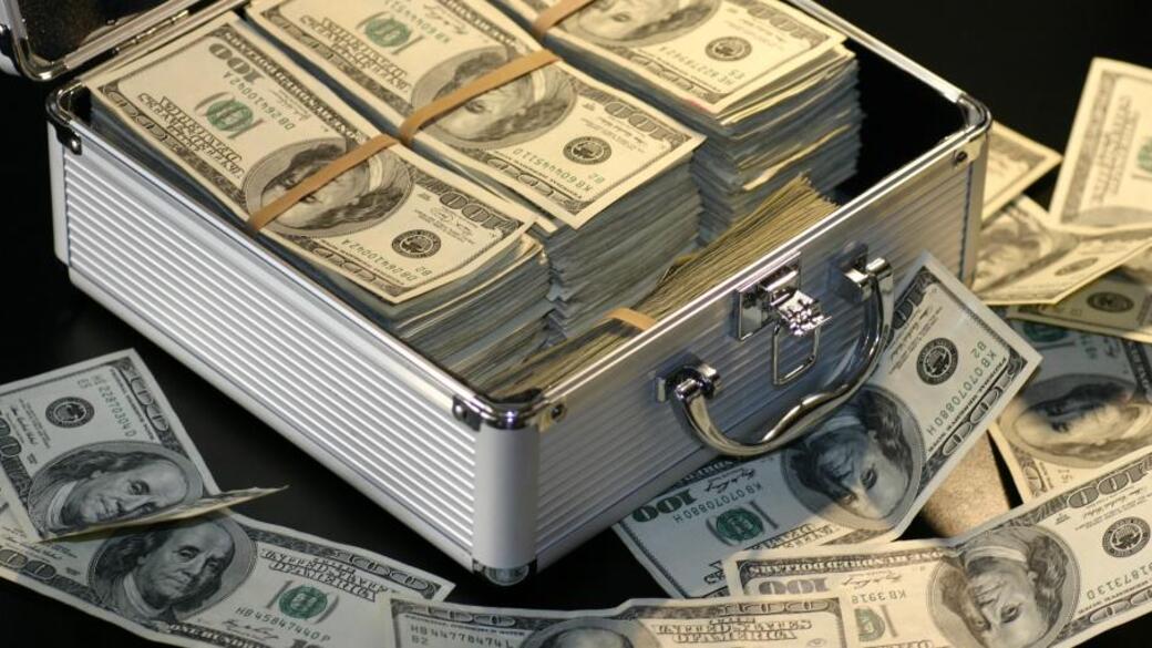 Briefcase filled with stacks of U.S. hundred-dollar bills, scattered banknotes around.