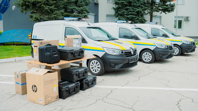 Four white vans parked near a building, with equipment cases and boxes in the foreground.