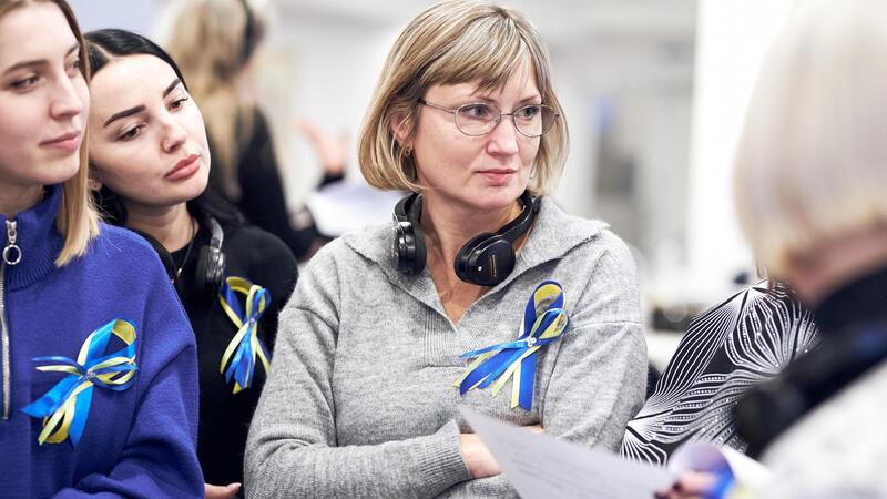 Women with blue and yellow ribbons gather, one holds a paper.