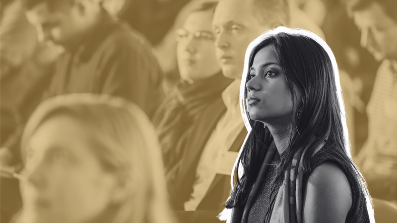 Young woman highlighted in focus surrounded by blurred audience, all attending a conference.